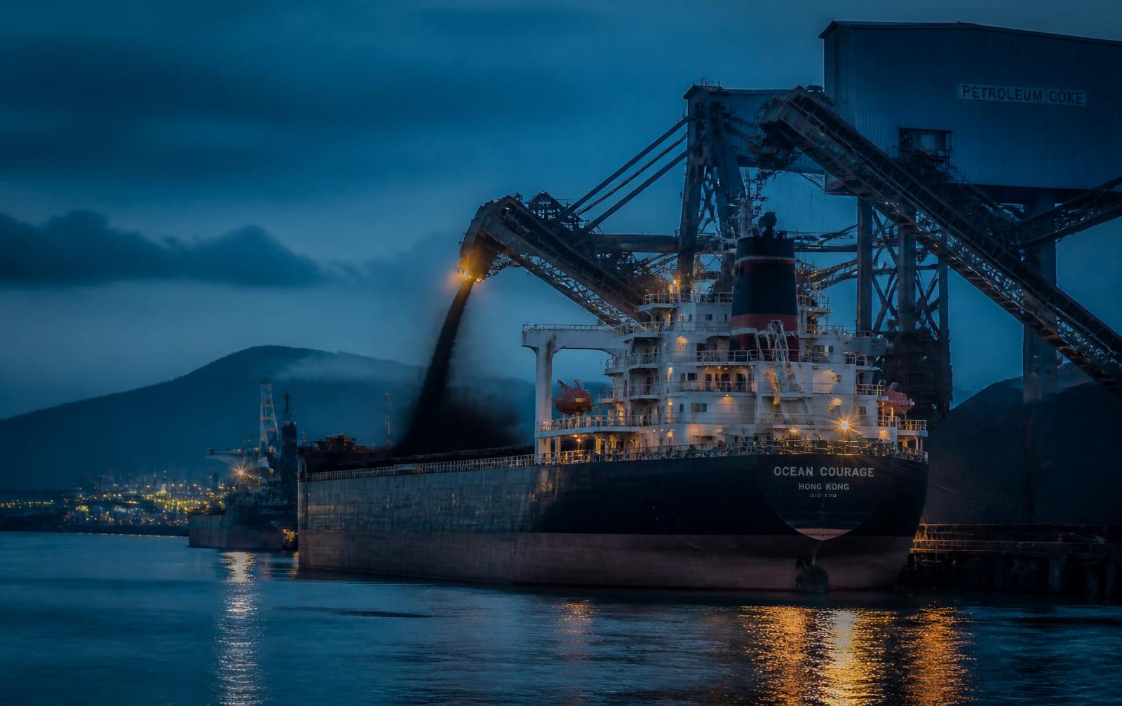 Bulk carrier loading petroleum coke at a port terminal at dusk